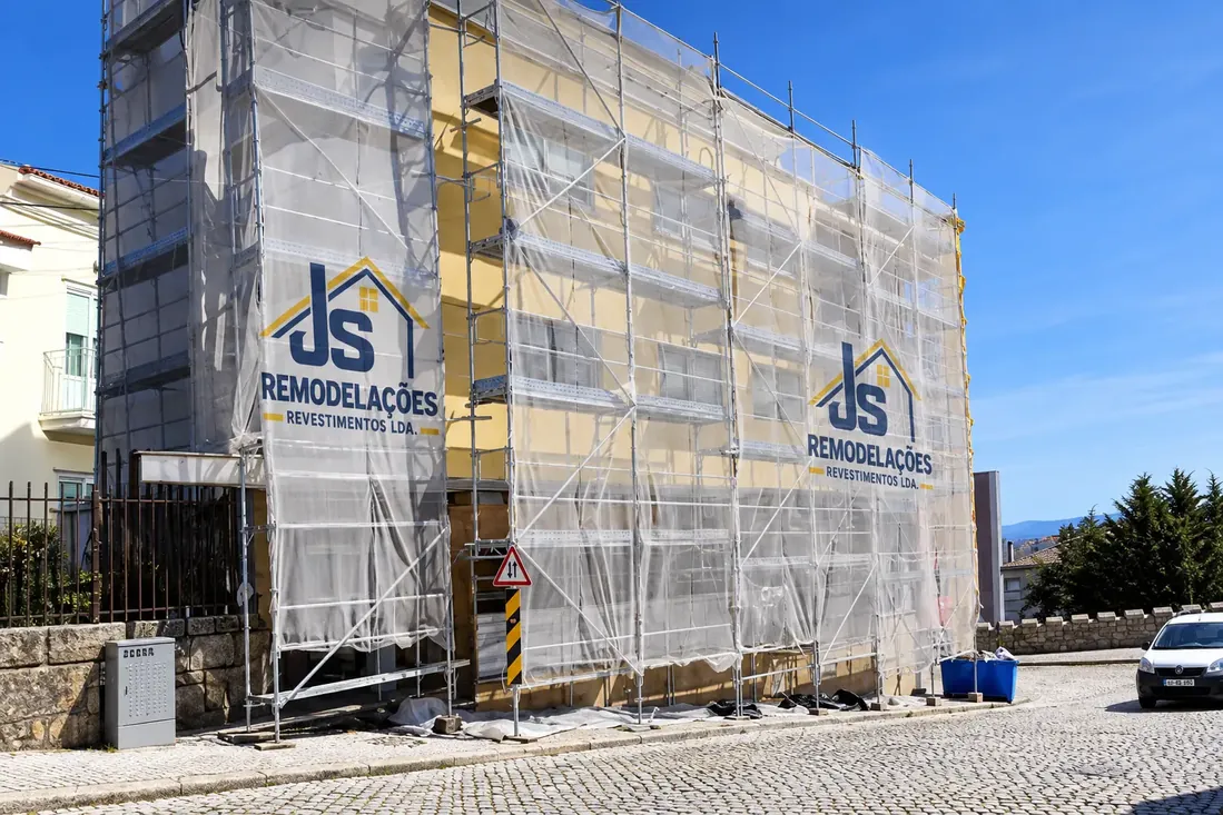 Revestimento de fachada em edifício protegido por tela de obra.